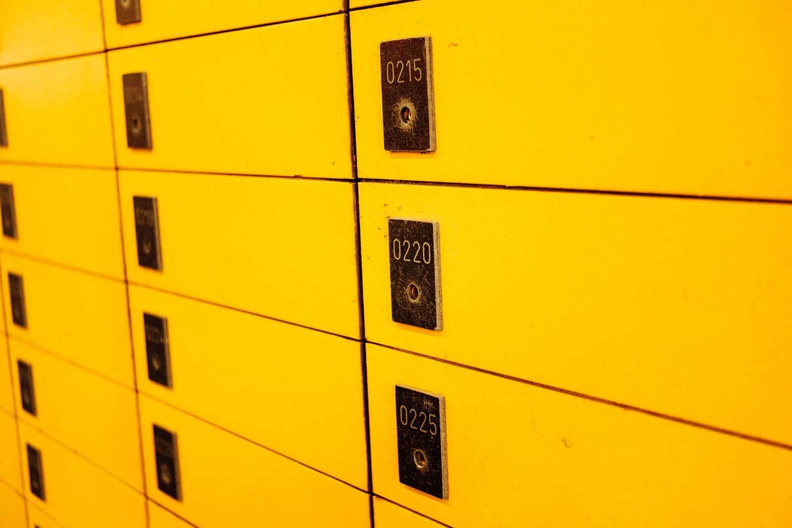 Parede de portas de armário numeradas com fechaduras metálicas, em tom amarelo