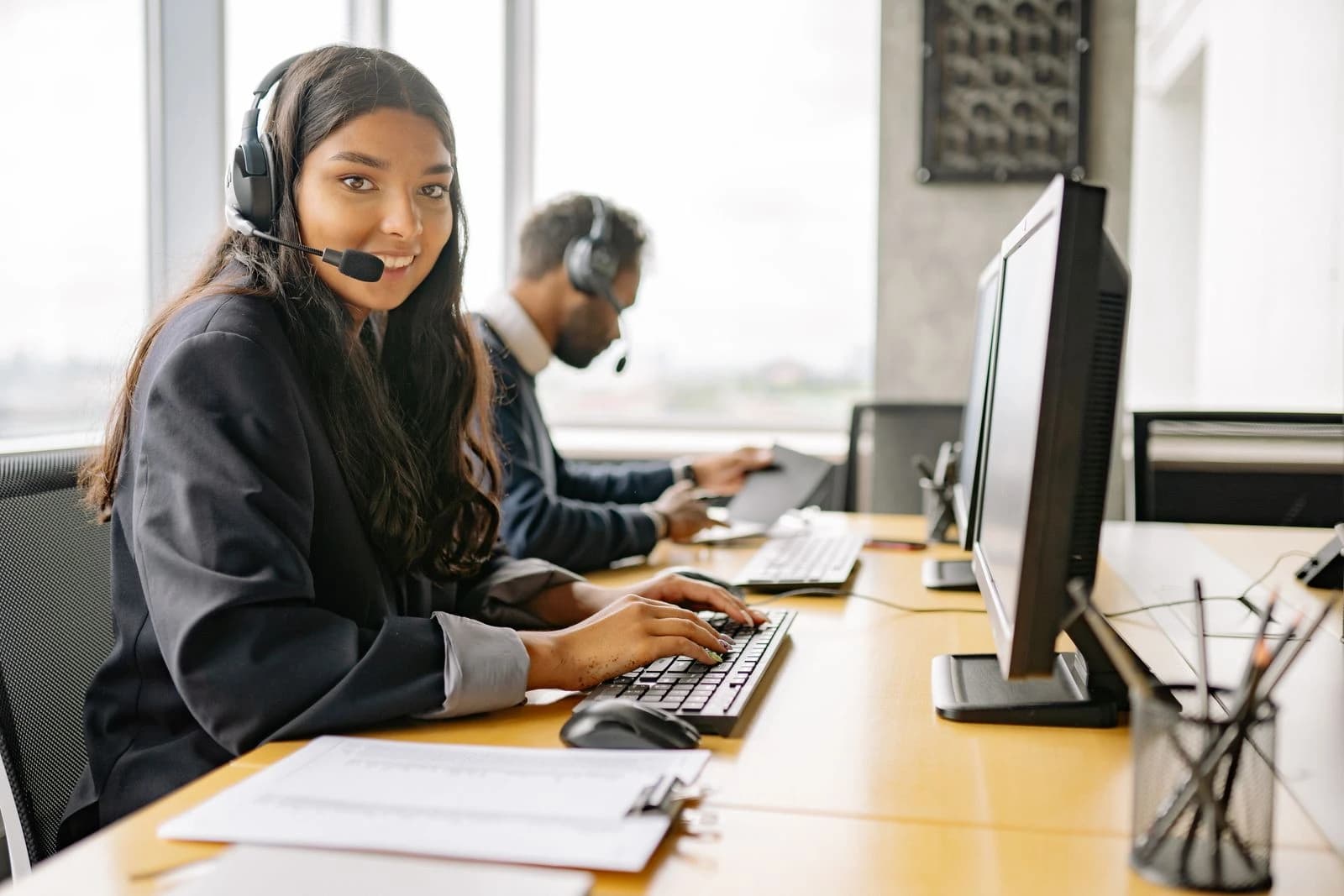 Atendente de suporte sorrindo, com headset, em frente ao computador